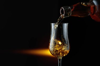 Şişeden bardağa güçlü bir alkollü içecek dökülüyor. Siyah arka planda keskin nişancı. Boşluğu kopyala.