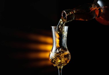 Şişeden bardağa güçlü bir alkollü içecek dökülüyor. Siyah arka planda keskin nişancı. Boşluğu kopyala.