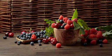 Bahçedeki eski ahşap bir masada çilek, yabanmersini, ahududu ve tatlı kiraz karışımının yakın plan renkli meyveleri. Yapraklı çeşitli meyveler.