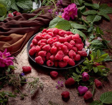 Siyah tabakta taze sulu ahududular. Yaz ayları, ahududular, çiçekler ve çayır otlarıyla geçer.. 