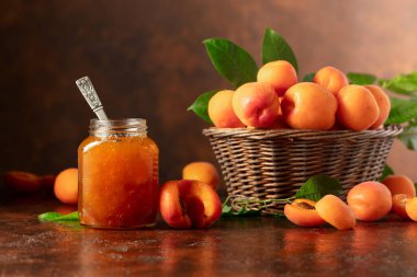 Cam kavanozda kayısı reçeli ve kahverengi bir masada taze meyve. Boşluğu kopyala.