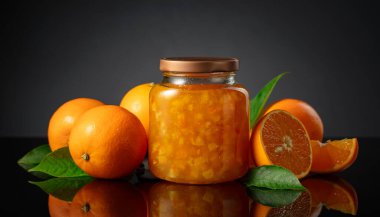 Cam kavanozda portakal reçeli ve taze meyve. Siyah yansıtıcı arka planda tatlı bir kesişme.