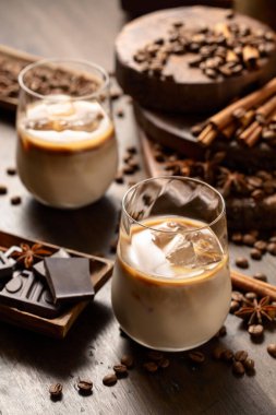 Eski ahşap arka planda buzlu bardakta İrlanda kreması ve kahve kokteyli. Kahve çekirdekleri, tarçın, anason ve çikolata parçaları masaya saçıldı.. 