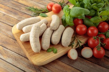 Geleneksel Bavyera beyaz sosisleri fesleğen ve domatesli ahşap kesim tahtasında.
