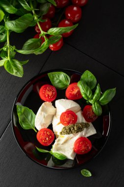 Taze fesleğenli Mozzarella, sulu vişneli domates ve siyah tabakta canlı pesto sosu. İtalya 'nın klasik bir tadı, güzel düzenlenmiş. Üst görünüm.