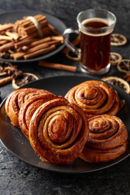 Kanelbullar - İsveç tarçınlı çörekler ya da dürümler. Siyah taş bir masada taze pişmiş çörekler..