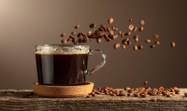 Eski bir tahtanın üzerinde cam bardakta sade kahve. Kavrulmuş kahve çekirdekleri hareket halinde. Boşluğu kopyala.