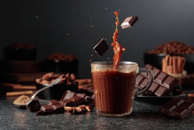 Siyah mutfak masasının üzerinde malzemeler olan bir bardak sıcak çikolata. Kakao parçacıkları bir bardak kakao içeceğinin içine düşer ve güzel bir su sıçratır..