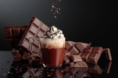 Krem şantili ve çikolata kırıntısı serpiştirilmiş sıcak çikolata. Arka planda kırık bir çikolata parçasında. Siyah yansıtıcı arkaplan.