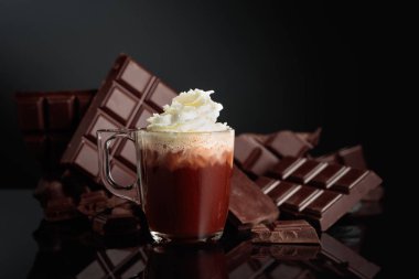 Krem şantili sıcak çikolata. Arka planda kırık bir çikolata parçasında. Kopyalama alanı olan siyah yansıtıcı arkaplan.