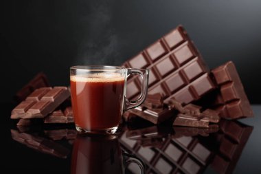 Bir bardak sıcak çikolata ve kırık acı çikolata. Kopyalama alanı olan siyah yansıtıcı arkaplan.