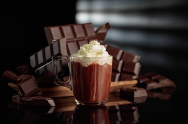 Kırık çikolatalara karşı krem şantili sıcak çikolata. Siyah parlak arka plan derinlik ve yansıma ekler. Boşluğu kopyala.