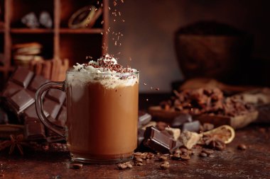 Üzerine krem şanti ve çikolata parçacıkları serpiştirilmiş çikolata içeceği. Eskimiş kahverengi arka planda yer alan malzemeler içeren bir çikolata içeceği..