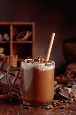 Üzerine krem şanti ve çikolata parçacıkları serpiştirilmiş çikolata içeceği. Eskimiş kahverengi arka planda yer alan malzemeler içeren bir çikolata içeceği..