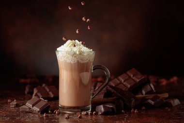 Krem şantili sıcak çikolata içeceği. Cam bardakta kakao ve koyu kahverengi arka planda acı çikolata..
