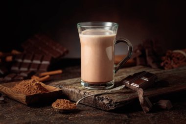 Kahverengi arka planda kremalı sıcak çikolata içeceği. Bir kupa sıcak çikolata, kırık çikolata ve kakao tozu. Boşluğu kopyala.