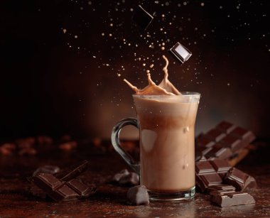 Acı çikolata parçaları cam bardağa dökülür kakao içeceği ile güzel su sıçratır. Boşluğu kopyala.