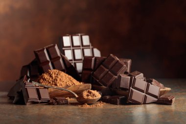 Tahta bir kase kakao tozunun yanında koyu çikolata kırıntıları. Sıcak kahverengi arka plan çikolata renginin zenginliğini vurgular. Boşluğu kopyala.