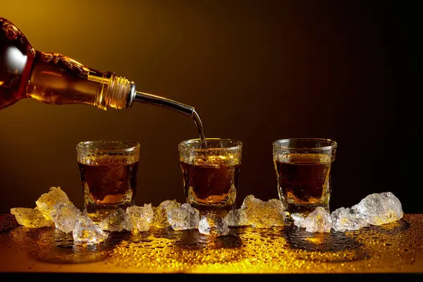 Viski şişeden cama doluyor. Viski ve buz siyah bir masada. Sarı ışık güzel gölgeler yaratır. Boşluğu kopyala.