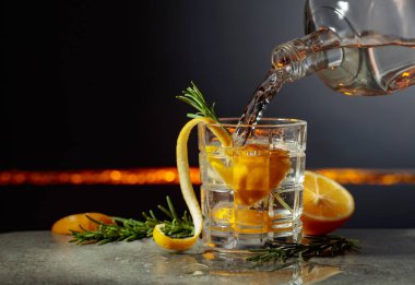 Limon ve biberiyeli cin tonik kokteyli. İçki şişeden buzlu bir bardağa dökülür. Boşluğu kopyala.