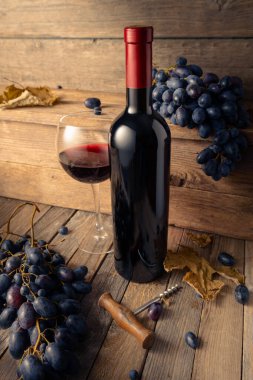 Eski ahşap bir masada mavi üzümlü bir şişe ve bir bardak kırmızı şarap..