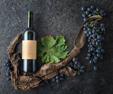 Bir şişe kırmızı şarap, mavi üzüm ve siyah taşlı arka planda eski asma parçaları. Eski boş bir şişede. Üst Manzara. Boşluğu kopyala.