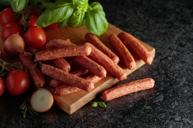 Siyah taş bir masada fesleğen, soğan, biberiye ve domatesli sosisler. Boşluğu kopyala.