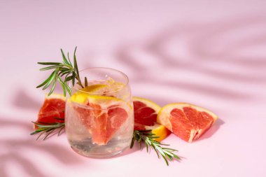 Buzlu, greyfurtlu ve biberiyeli yaz içeceği. Serin, gevrek ve pembe arka planda palmiye gölgeleri tarafından öpülmüş. Boşluğu kopyala.