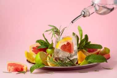 Buzlu, narenciyeli, biberiyeli ve naneli kokteyl. Cin veya rom şişeden bardağa dökülür. Kopya alanı ile pembe arkaplan.