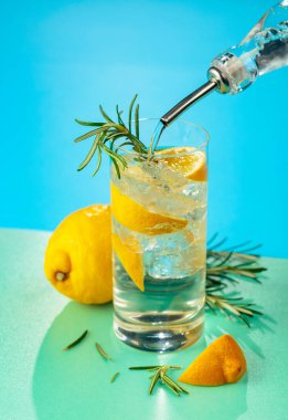 Cin, tonik, limon ve biberiyeyle taze kokteyl. Buzda servis ediliyor, renk ve tazelikle dolup taşıyor. Parlak renkli arkaplan.