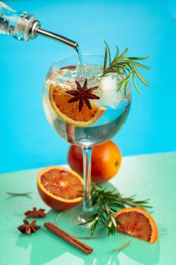 Cin, tonik, kan portakalı, tarçın, anason ve biberiyeli yaz kokteyli. Buzda servis ediliyor, renk ve tazelikle dolup taşıyor. Parlak renkli arkaplan.
