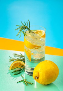 Cin, tonik, limon ve biberiyeyle taze kokteyl. Buzda servis ediliyor, renk ve tazelikle dolup taşıyor. Parlak renkli arkaplan.