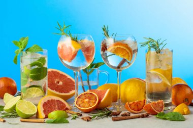 Beyaz mermer bir masada malzemelerle yaz kokteyllerini tazeliyorum. Mojito ve mavi arka planda çeşitli cin tonik kokteylleri..