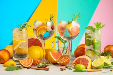 Beyaz mermer bir masada malzemelerle yaz kokteyllerini tazeliyorum. Mojito ve çeşitli cin tonik kokteylleri parlak renkli bir arka planda..