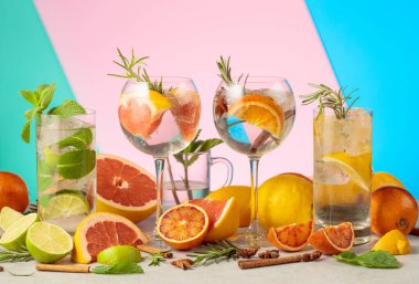 Beyaz mermer bir masada malzemelerle yaz kokteyllerini tazeliyorum. Mojito ve çeşitli cin tonik kokteylleri parlak renkli bir arka planda..