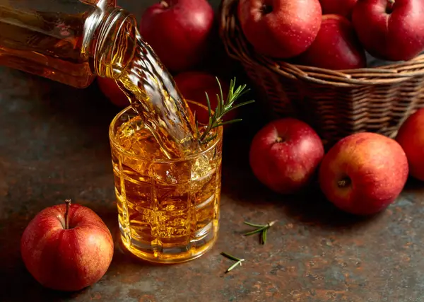 Elma suyu şişeden bardağa dökülür. Bir bardak meyve suyu ve taze elma eski bir mutfak masasında oturuyor..