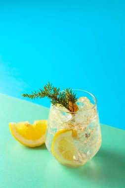 Ezilmiş buz, limon dilimleri ve ardıç dalıklı cin tonik kokteyli. Yeşil-mavi arka planda yaz ferahlatıcı içecek. Boşluğu kopyala.