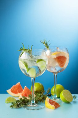 Kokteyller, greyfurtlu cin tonik ve mavi arka planda limon dilimleri..