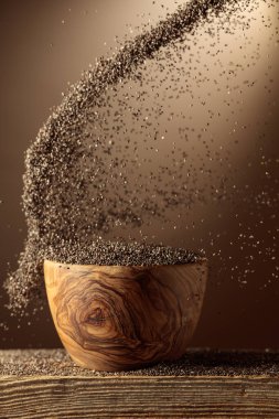 Chia tohumları ahşap bir kaseye dökülür. Kopyalama alanı olan bej arkaplan.