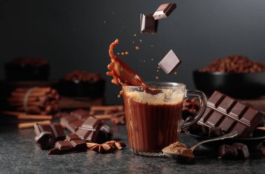 Siyah mutfak masasının üzerinde malzemeler olan bir bardak sıcak çikolata. Kakao parçacıkları bir bardak kakao içeceğinin içine düşer ve güzel bir su sıçratır..