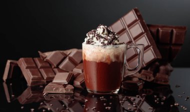 Krem şantili ve çikolata kırıntısı serpiştirilmiş sıcak çikolata. Arka planda kırık bir çikolata parçasında. Siyah yansıtıcı arka plan. Boşluğu kopyala.