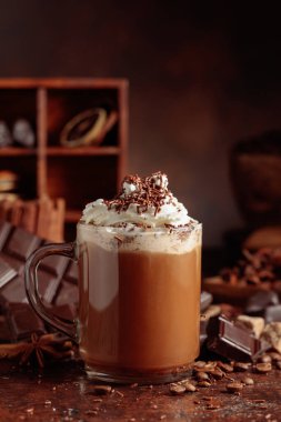 Üzerine krem şanti ve çikolata parçacıkları serpiştirilmiş çikolata içeceği. Eskimiş kahverengi arka planda yer alan malzemeler içeren bir çikolata içeceği..