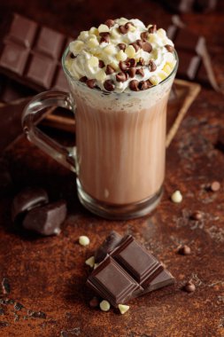 Krem şantili sıcak çikolata içeceği. Cam bardakta kakao ve koyu kahverengi arka planda acı çikolata..