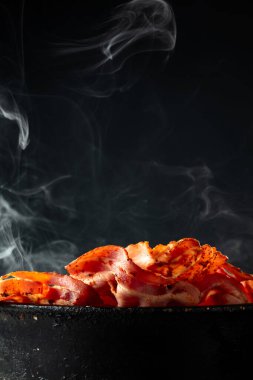 Siyah arka planda eski siyah bir tavada buharda pişmiş domuz pastırması. Boşluğu kopyala.