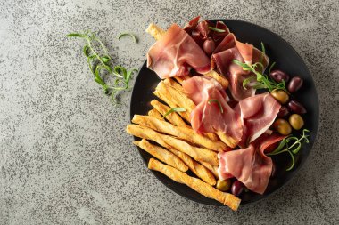 Siyah tabakta ekmek çubuğu, zeytin ve biberiyeli jambon. Geleneksel İtalyan atıştırmalıkları. Üst görünüm.