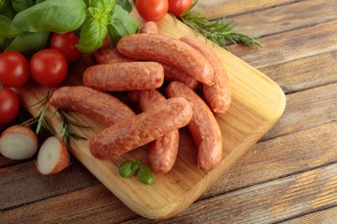 Tahta kesme tahtasının üzerinde fesleğen ve domatesli sosisler..