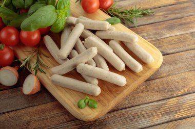 Geleneksel Bavyera beyaz sosisleri fesleğen ve domatesli ahşap kesim tahtasında.