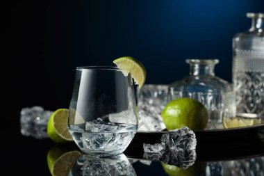 Buzlu bir bardakta cin. Siyah yansıtıcı arka planda ezilmiş buz ve limon dilimleri.