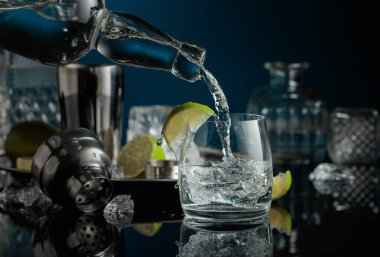 Votka ya da cin buzlu bir bardağa doldurulur. Siyah yansıtıcı arka planda ezilmiş buz ve limon dilimleri.