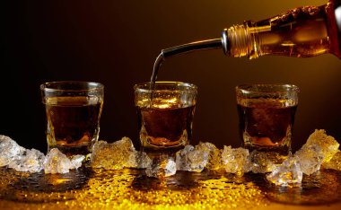 Viski şişeden cama doluyor. Viski ve buz siyah bir masada. Sarı ışık güzel gölgeler yaratır. Boşluğu kopyala.